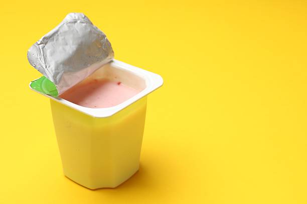 Delicious yogurt in plastic cup on yellow background, closeup. Space for text