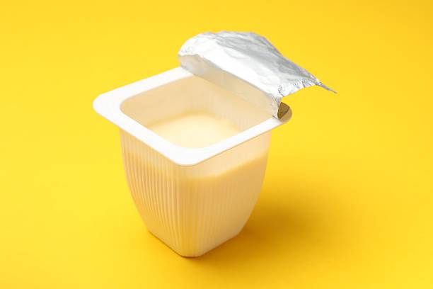 Delicious yogurt in plastic cup on yellow background, closeup