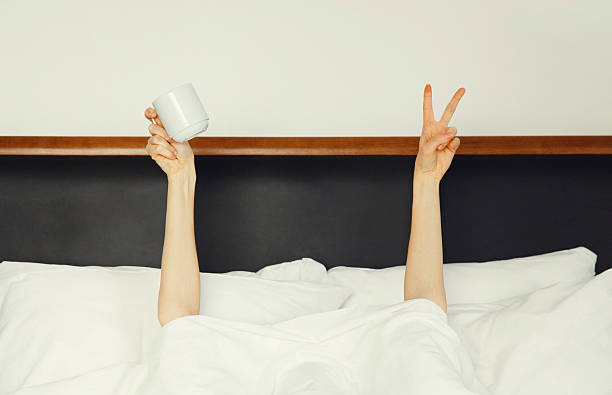 istock Cheerful lazy woman waking up after sleeping lying in bed holding cup in her hands asks for coffee 2215186701