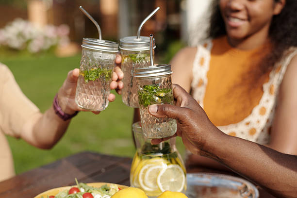 Group of friends enjoying refreshing mint lemonade outdoors during warm sunny day, sharing happy moment with drinks and light snacks visible in foreground