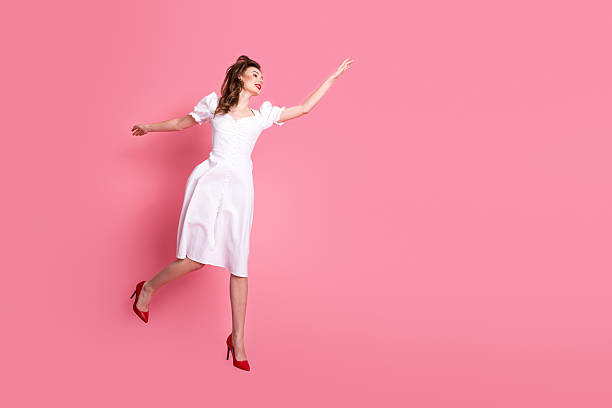 istock Charming young woman in a white dress posing elegantly while gesturing with her hand against a vibrant pink background 2215188472