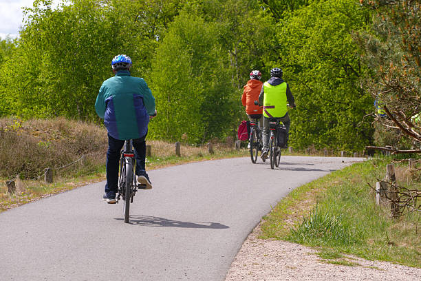 Hamburg, Germany May 8. 2025: Three cyclists seen from behind on a paved bike path through green spring landscape. The riders wear helmets and colorful clothing. The scene was captured on a sunny day.