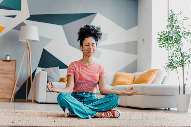 istock Young woman practicing mindfulness while meditating in cozy apartment living room during a sunny day 2215188614