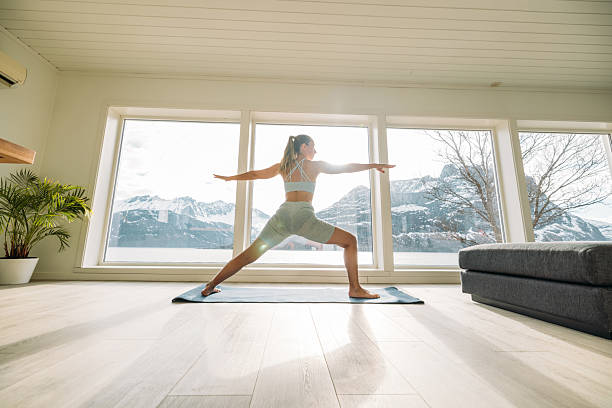 istock Woman Practicing Yoga Warrior Pose in Sunlit Room 2215190039