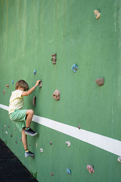 Child practicing rock climbing on a green climbing wall
