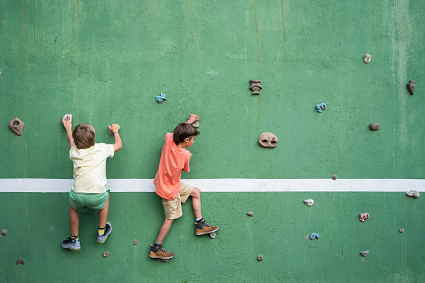 Two young boys climbing a green climbing wall, having fun at the playground