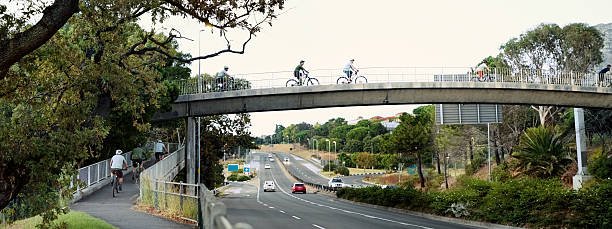 istock Cyclists biking on bridge over road surrounded by trees 2215191912
