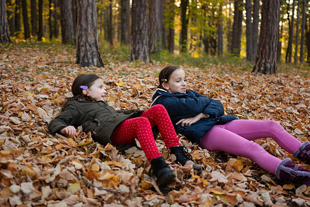 Two happy girls having fun lying in autumn leaves in the forest