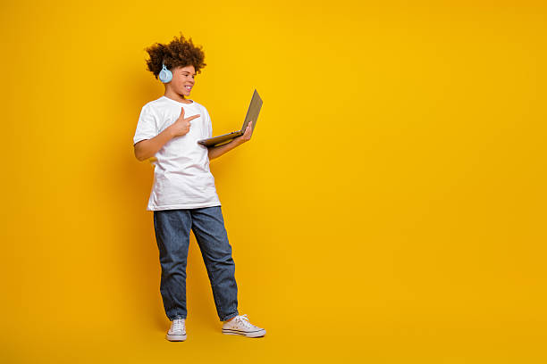 istock Smiling young boy wearing headphones with a laptop against bright yellow background studious modern lifestyle concept 2215194562