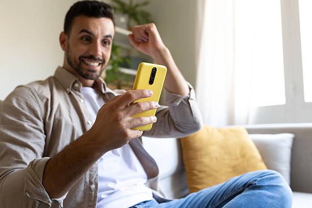 istock Excited young man celebrating success on smartphone at home 2215203614