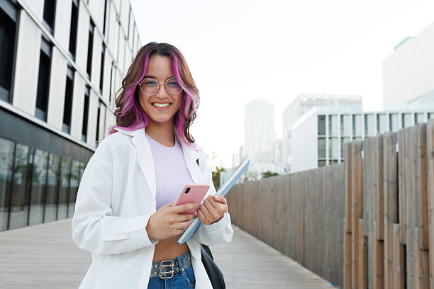 istock Smiling student using smartphone and holding notebooks near university campus 2215204698