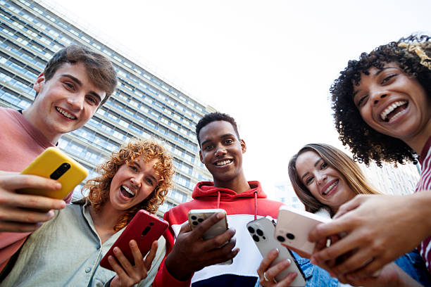 istock Happy students using smartphones in university campus: low angle view of cheerful diverse friends enjoying mobile technology 2215204707