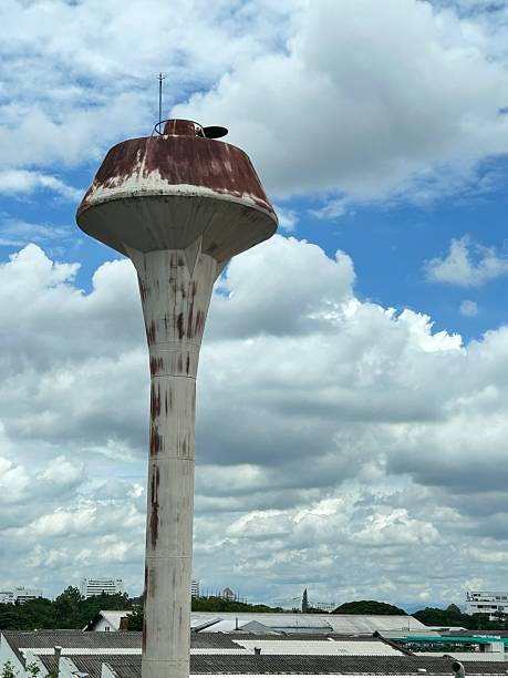 An old, rusty water tower stands tall above the rooftops, set against a partly cloudy sky