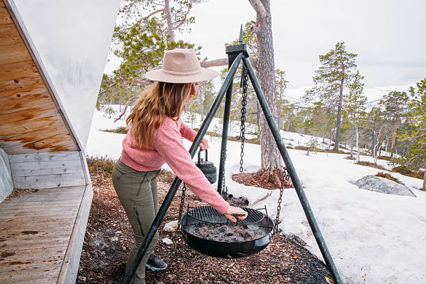 istock Woman in Winter Forest Preparing Campfire Kettle on Tripod 2215206357