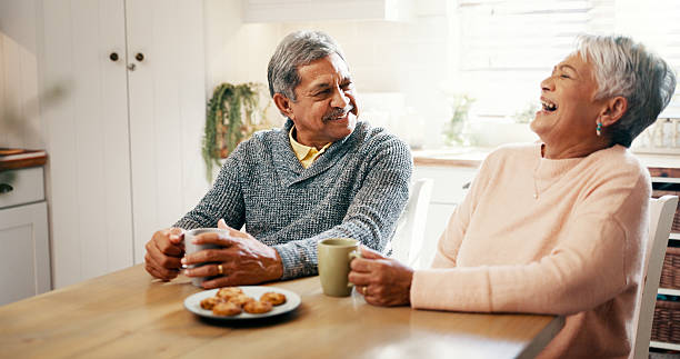 istock Home, old couple and breakfast with tea for laughing, bonding and biscuits with talking in retirement. Senior people, woman and man with smile for love, funny joke and cookies with coffee in kitchen 2215207093