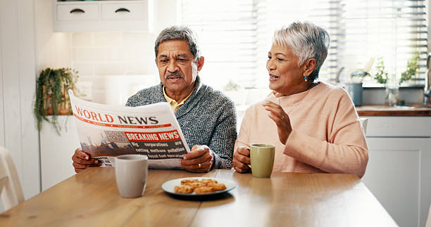 istock Senior couple, newspaper and coffee in kitchen, discussion and breakfast with headline, update and story. Elderly man, woman and talk with tea cup, article or newsletter with bonding in retirement 2215207109