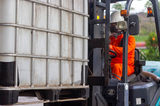 istock A worker in high visibility orange gear operates a forklift transporting a large white industrial container. 2215208725