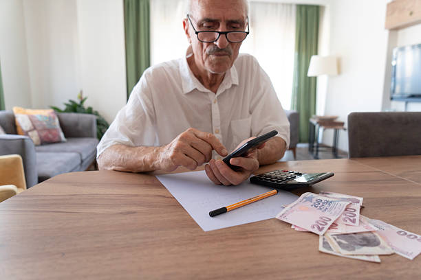 istock Senior man managing finances, holding cash and using calculator at home 2215211362