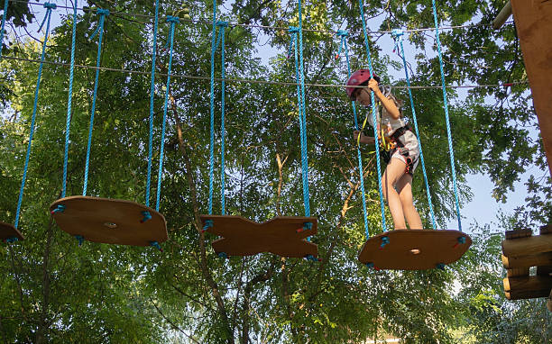 A young girl balances on swinging wooden platforms high above the ground.