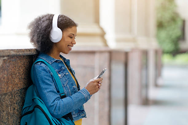 istock Smiling black female student listening music andusing smartphone while relaxing at campus 2215214460