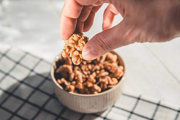 istock Woman's hand holding a walnut kernel above a bowl filled with walnuts, preparing to savor a nutritious and delicious snack packed with protein and healthy fats 2215217012