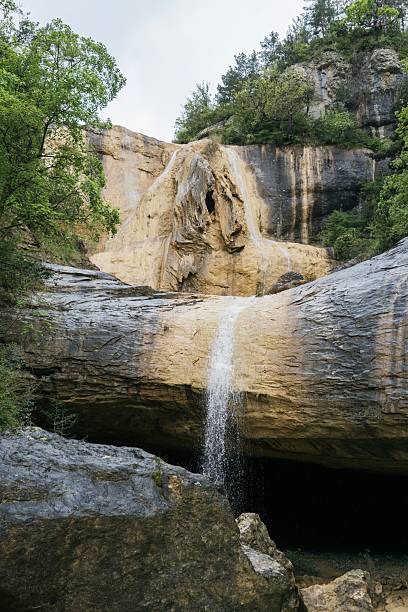 istock Secluded waterfall cascading into turquoise grotto pool. Limestone cave formation with crystal clear water creating hidden swimming hole beneath towering rock cliffs. Pozas San Martin, Huesca 2215217232