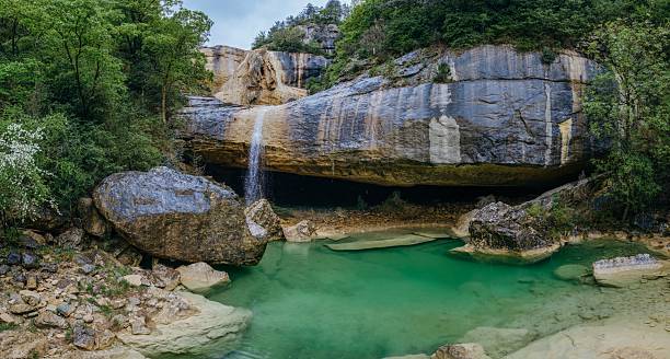 istock Hidden limestone grotto with waterfall and turquoise pool. Natural cave formation creating secluded swimming basin beneath towering rock walls in wilderness setting. Pozas de San Martin, Huesca 2215217234