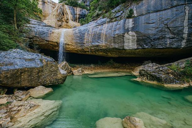 istock Enchanting cave waterfall flowing into pristine jade pool. Natural limestone grotto with emerald waters forming secret swimming hole beneath massive rock overhang. Pozas de San Martin, Huesca 2215217245