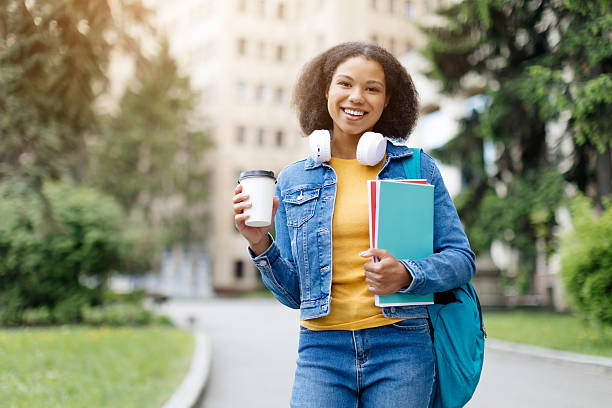 istock Smiling African American female student holding a takeaway coffee cup and notebooks 2215219109