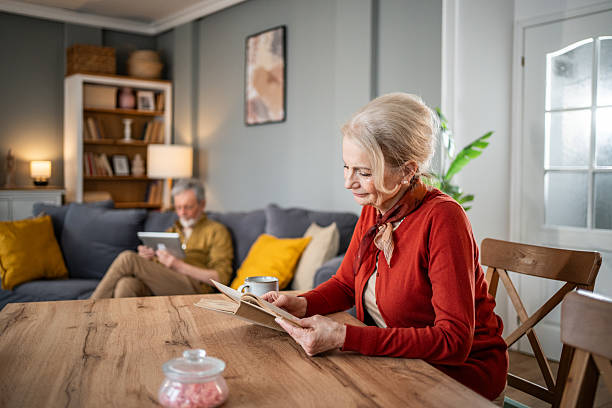 istock Senior woman reading a book while man uses digital tablet on sofa 2215224940