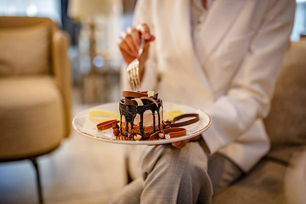 A young businesswoman sits in a stylish hotel lobby, savoring a decadent dessert while using her phone to manage travel arrangements for her upcoming business trip.