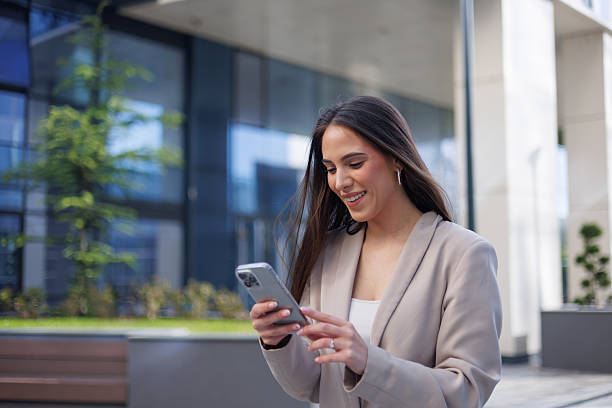 istock Young businesswoman smiling while using a smartphone outside a modern office building, enjoying a break and staying connected 2215236002