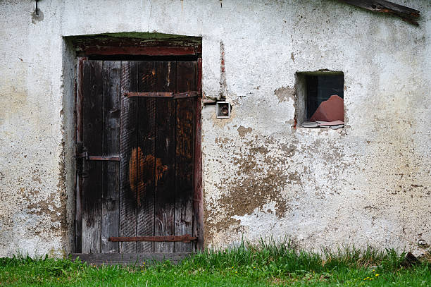 istock Old wooden door and small window on weathered wall 2215236447