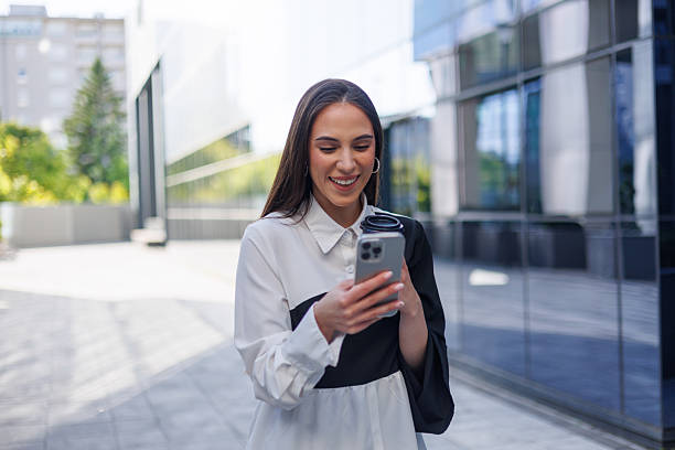 istock Young businesswoman walking outside an office building, smiling while using her smartphone, enjoying the vibrant city atmosphere 2215239966