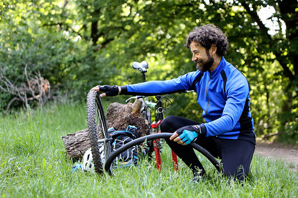 Male cyclist changing a  flat tire on a bicycle in a forest. About 40 years old, Caucasian man.