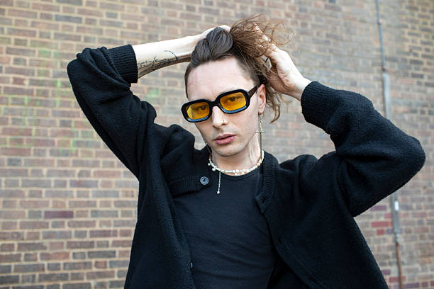 istock Fashionable young man with arms raised by a brick wall 2215246394