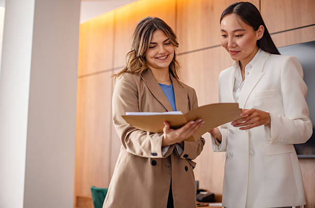 istock Young businesswomen holding a folder while discussing plans in a luxury hotel lobby setting 2215250801