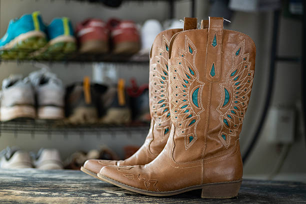 Leather patterned cowboy boots standing on the floor against a shoe shelf. Place for text.