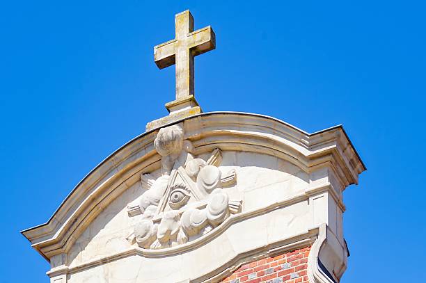 istock Stone cross standing above all-seeing eye symbol on building facade 2215261727