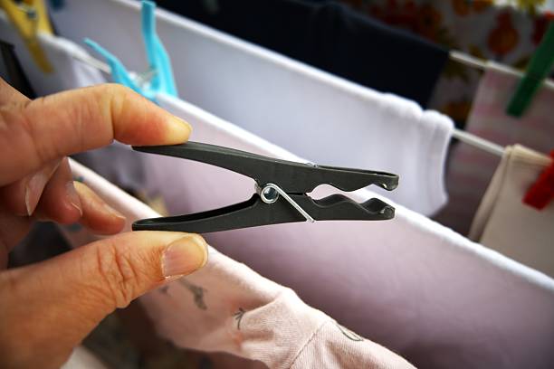 One gray plastic clothespin in hand with drying clothes