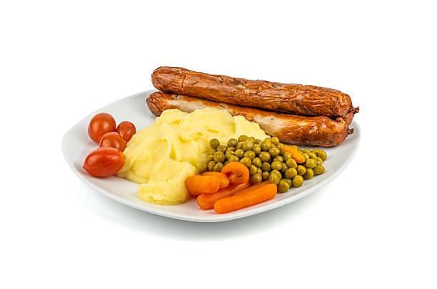 A plate with bratwurst, mashed potatoes, peas, carrots, and tomatoes. A hearty lunch with colorful vegetables. Plate with food isolated on white background