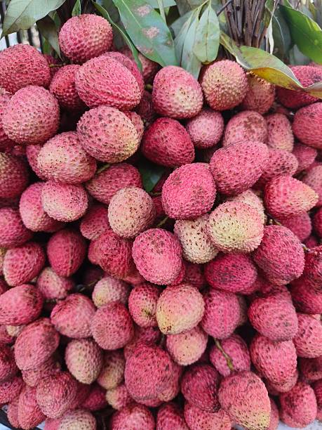 Ripe lychees spilling out of a small white bowl, with one open showing the flesh inside