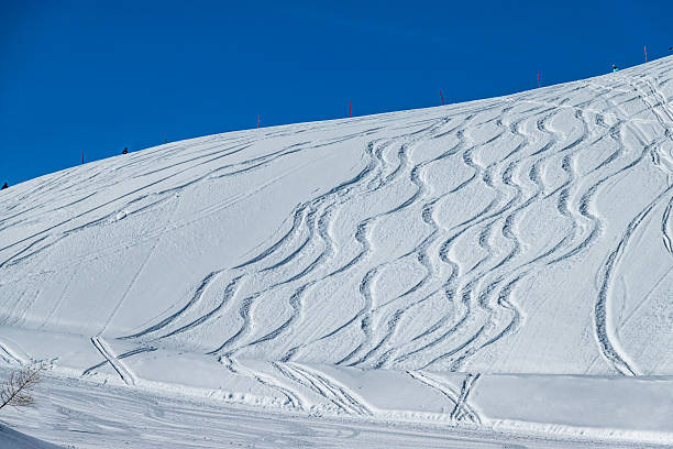 istock Fresh ski tracks create wavy patterns on a snow-covered slope in bright sunlight at a mountain resort during winter 2215275322