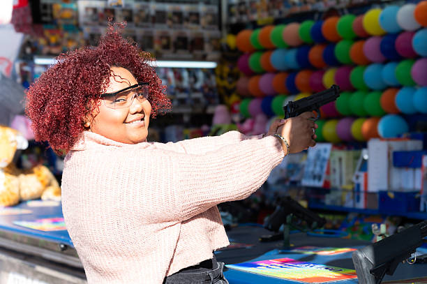 Young woman enjoying a vibrant fun fair, playfully aiming at targets while having fun in the shooting game under bright sunlight