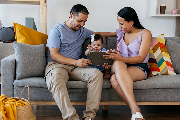 istock Hispanic family using tablet with baby daughter on sofa at home 2215283429