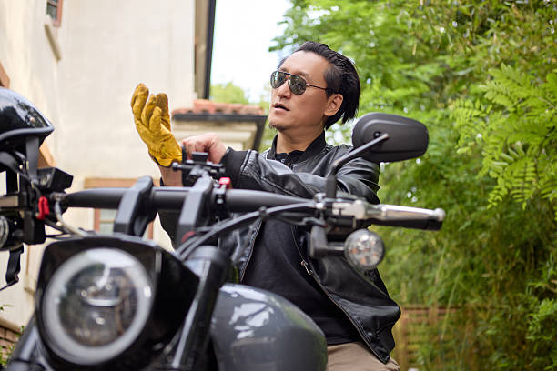 Mature man with sunglasses wearing biker jacket sitting on his motorcycle after a ride in the desert at sunset