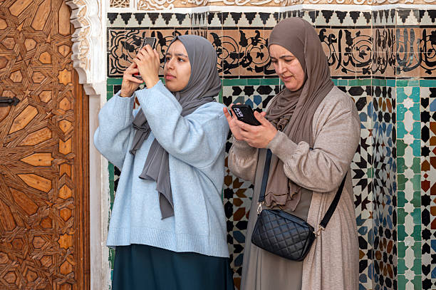 Marrakech, Morocco - February 18, 2025: Women admire the ornate details of Marrakech's architecture while using their phones.
