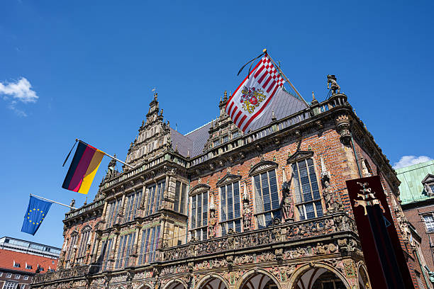 Die reich verzierte Frontfassade des historischen Rathauses in Bremen mit drei wehenden Flaggen vor blauem Himmel an einem sonnigen Tag
