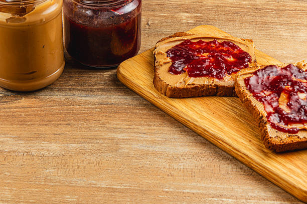Slices of bread spread with peanut butter and jelly sit on a wooden cutting board alongside jars of jelly and peanut butter, showcasing a classic snack.