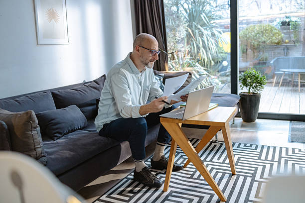 istock Mature man working on laptop and holding documents at home 2215302178